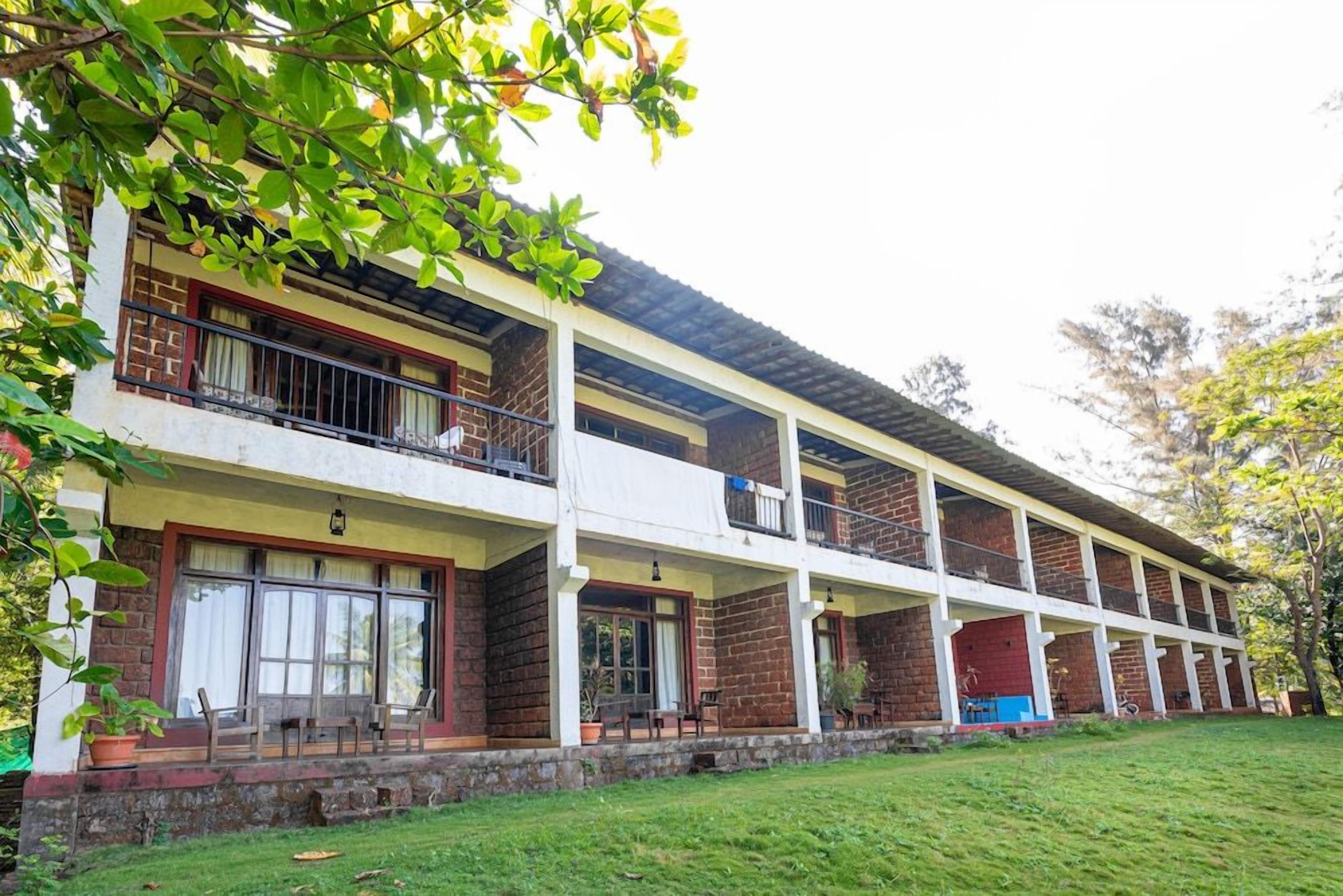 A multi-story building with balconies, a flat roof, and a grassy area in front.