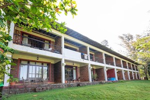 Un edificio de varios pisos con balcones, techo plano y un área verde al frente.