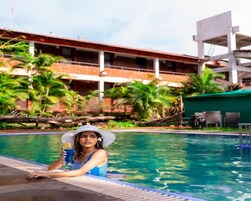 Uma pessoa relaxando à beira da piscina, com um edifício ao fundo.