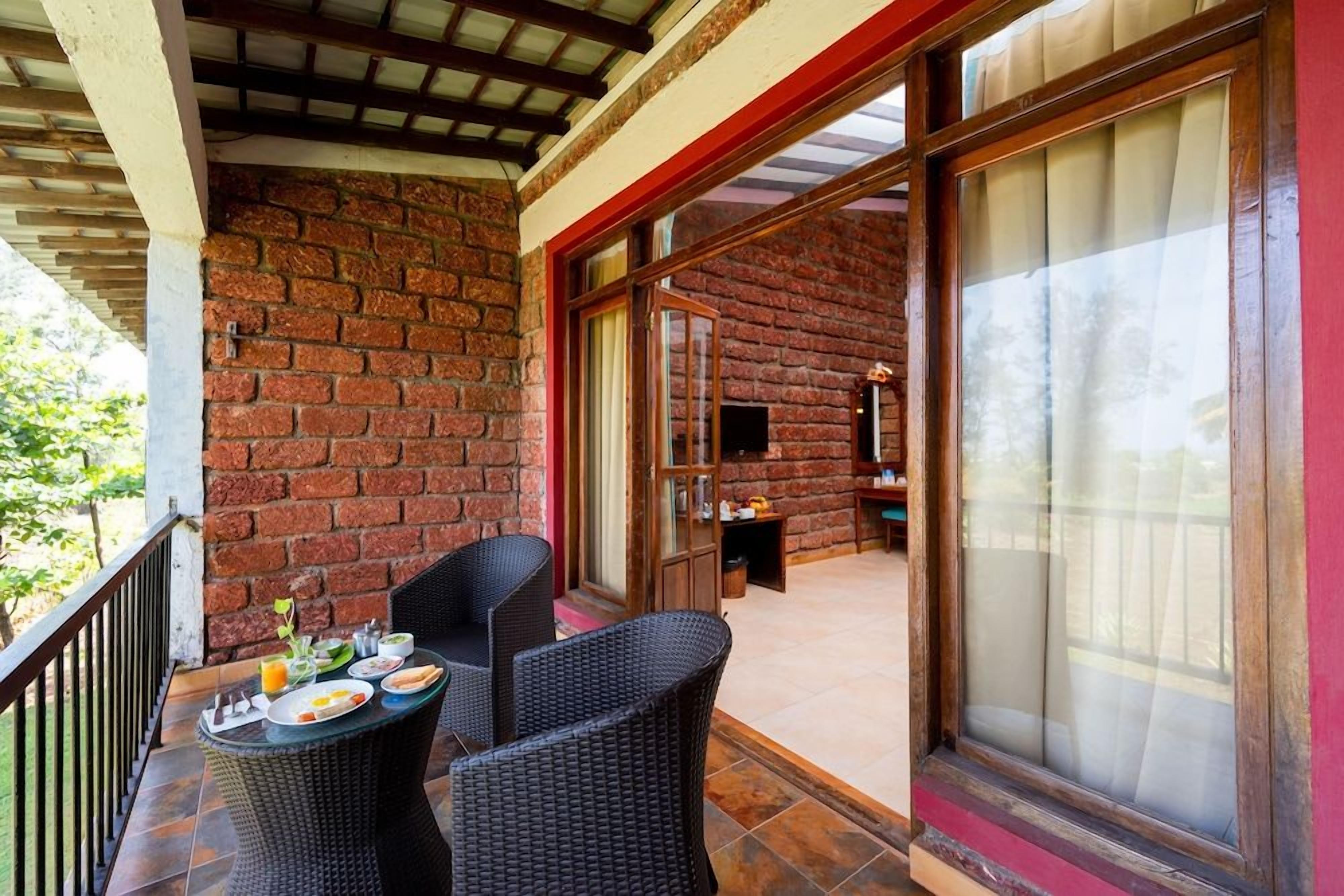 Een balkon met rieten meubels en een ontbijt-gedekte tafel, met uitzicht op een bakstenen muur en een glazen deur die naar een andere kamer leidt.