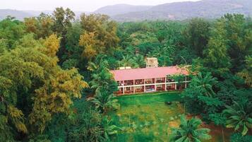 A large, single-story building with a red roof, surrounded by dense greenery and palm trees.