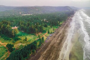 Vista aérea de uma área costeira com praia, vegetação densa e edifícios dispersos.