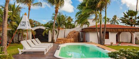 Un área de piscina con sillones reclinables, una piscina pequeña y palmeras.