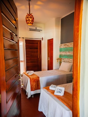 Une chambre d’hôtel avec deux lits, une armoire en bois, un luminaire suspendu et un climatiseur fixé au mur.