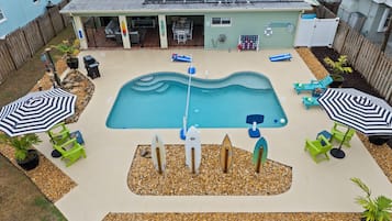 A backyard with a swimming pool, lounge chairs, and umbrellas.
