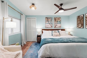 A bedroom with a bed, bedside tables, a ceiling fan, and artwork on the walls. - NEW! Retro Bungalow·Pool·Game Room·Walk to Beach (Cocoa Beach)