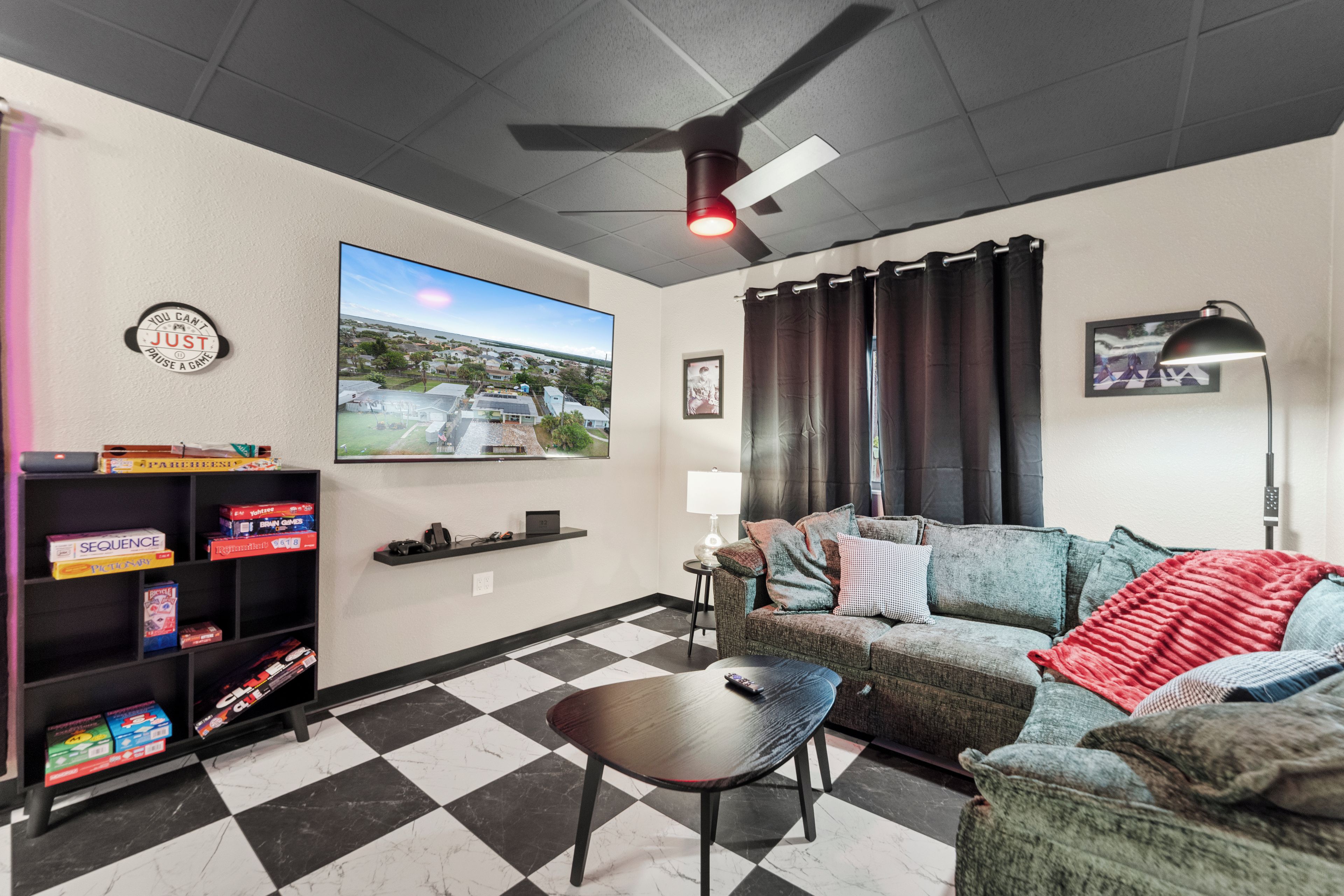 A living room with a checkered floor, a television mounted on the wall, a ceiling fan, a couch, and a coffee table.
