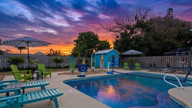 Un giardino con piscina, sedie verdi e un capanno blu.