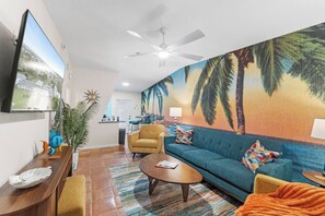 A living room with a sofa, armchair, coffee table, and a TV mounted on the wall. - NEW! Heated Pool·Retro Bungalow·Game Room·Walk to Beach (Cocoa Beach)