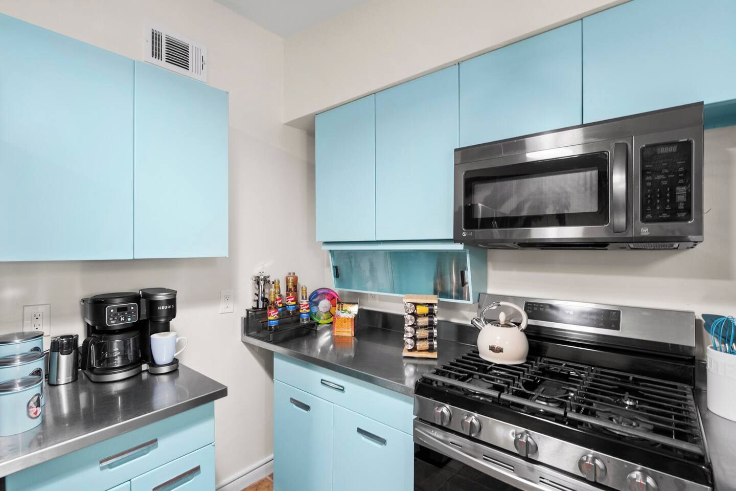 A modern kitchen with light blue cabinets, a stainless steel stove, a microwave, and a coffee maker.