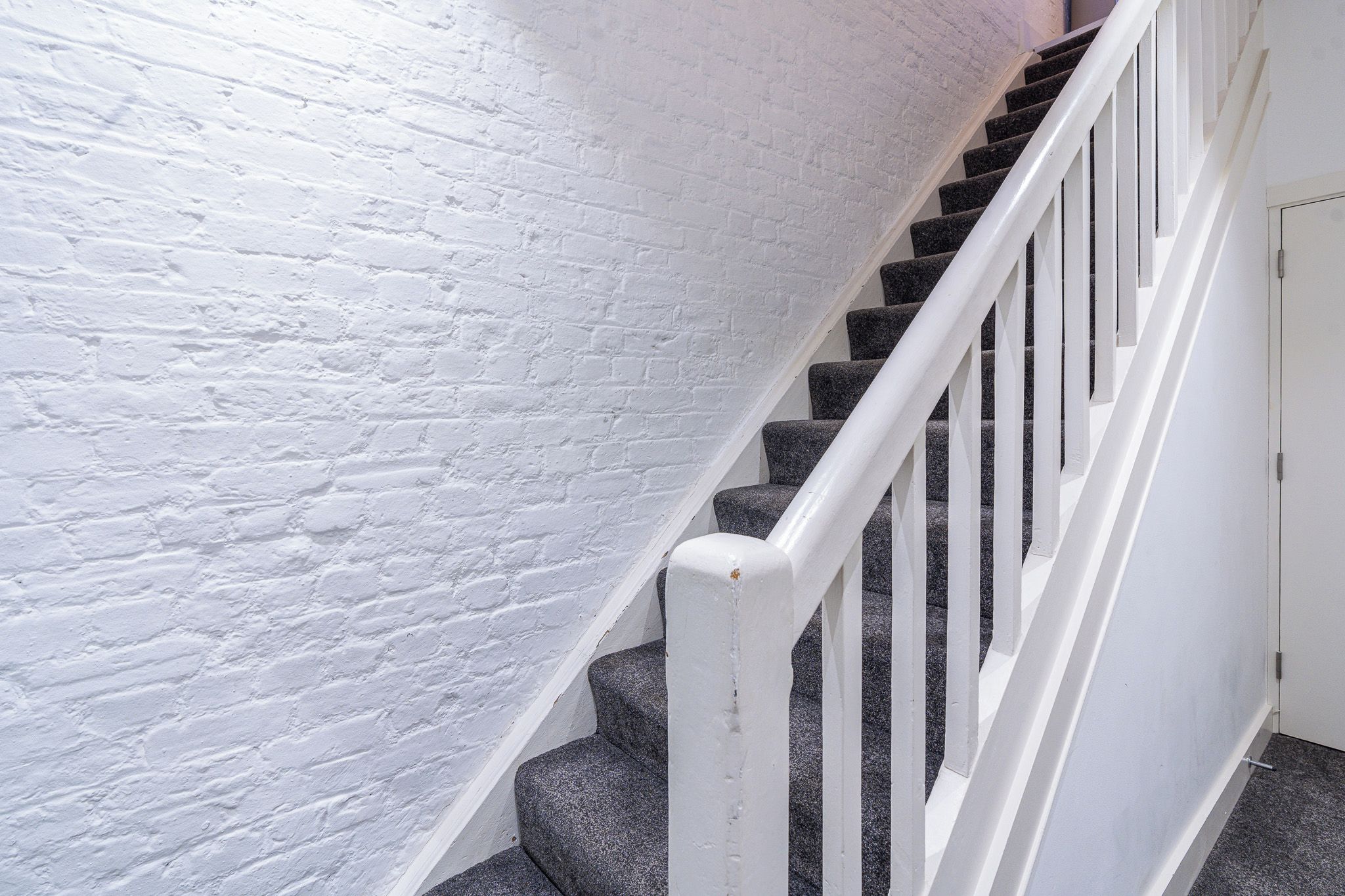 Un escalier avec des rampes blanches et un mur en briques blanches.