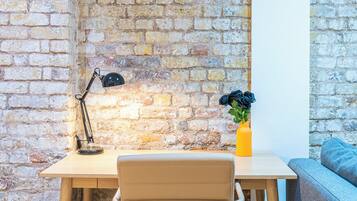 A corner office with a brick wall, a desk with a chair, a lamp, and a vase with flowers.