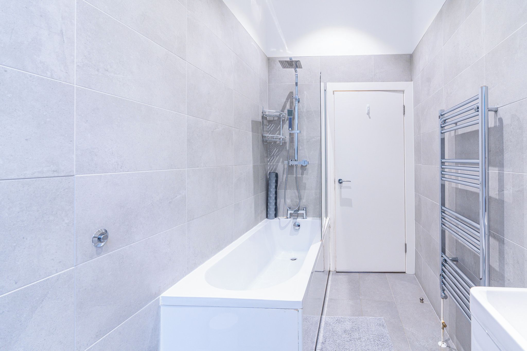 A modern bathroom with a white bathtub, a shower, and a towel rack.