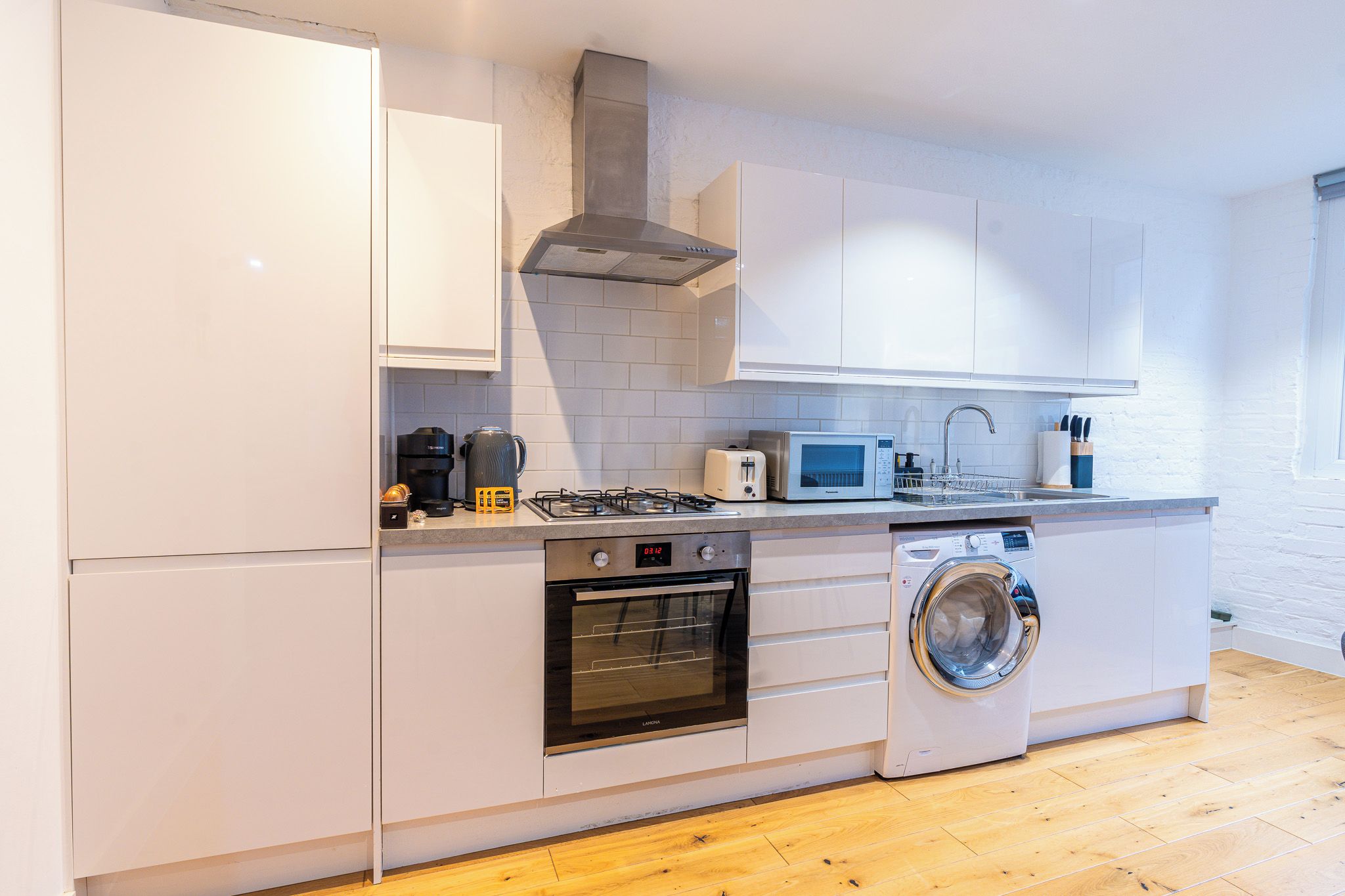 A modern kitchen with white cabinets, a built-in oven, a microwave, a gas stove, and a washing machine.