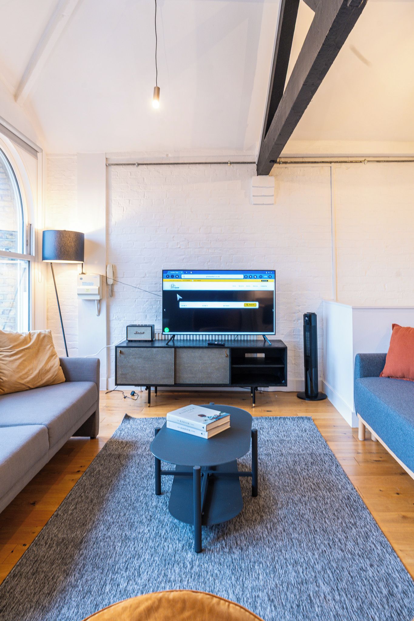A modern living room with a flat-screen TV, grey sofa, coffee table, and a grey rug.