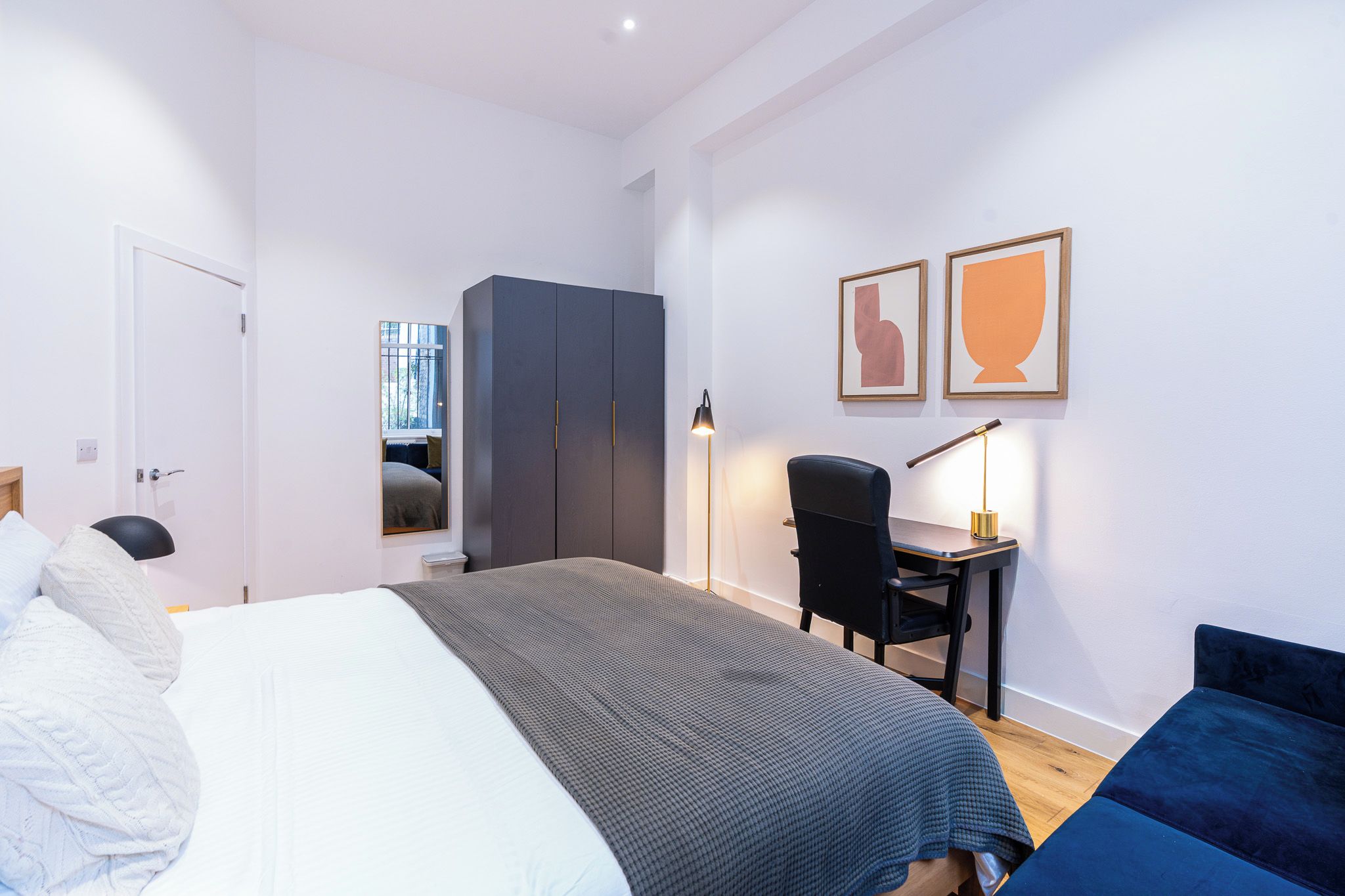 A modern hotel room with a large bed, a desk, and a wardrobe.