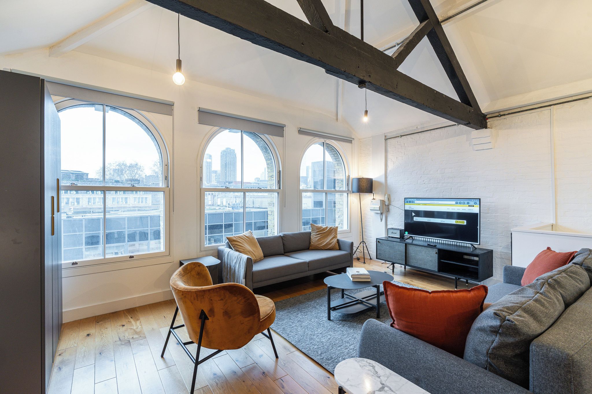 Una sala de estar moderna con ventanas amplias, un sofá gris, una mesa de centro y una televisión.