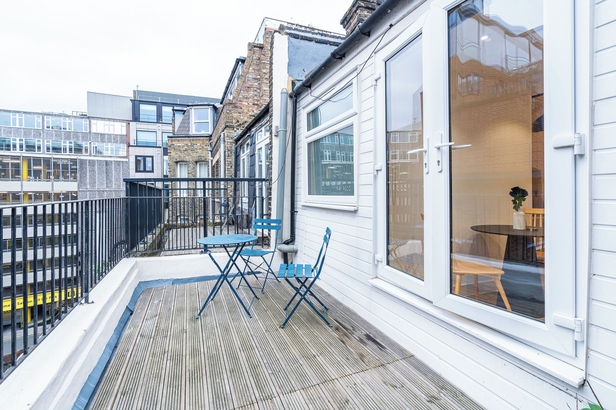 Un balcon avec une table et des chaises, une vue sur la rue et un immeuble doté de grandes fenêtres.