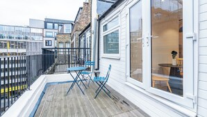 A balcony with a table and chairs, a view of the street, and a building with large windows. - Farringdon Residence (London)
