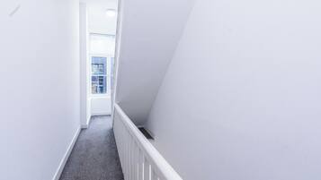 A narrow, white-walled hallway with a grey carpet and a white railing.
