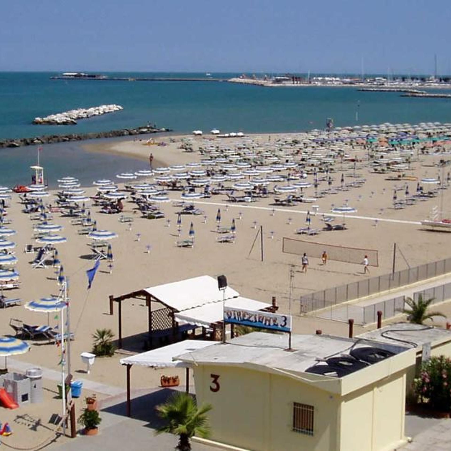 A beach with numerous umbrellas and sun loungers, a lifeguard tower, and a building labeled 'DANZAUARTE 3'.
