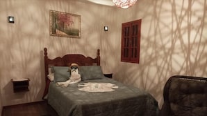 Quarto com cama, cadeira, mesa de cabeceira, luminária na parede e janela.