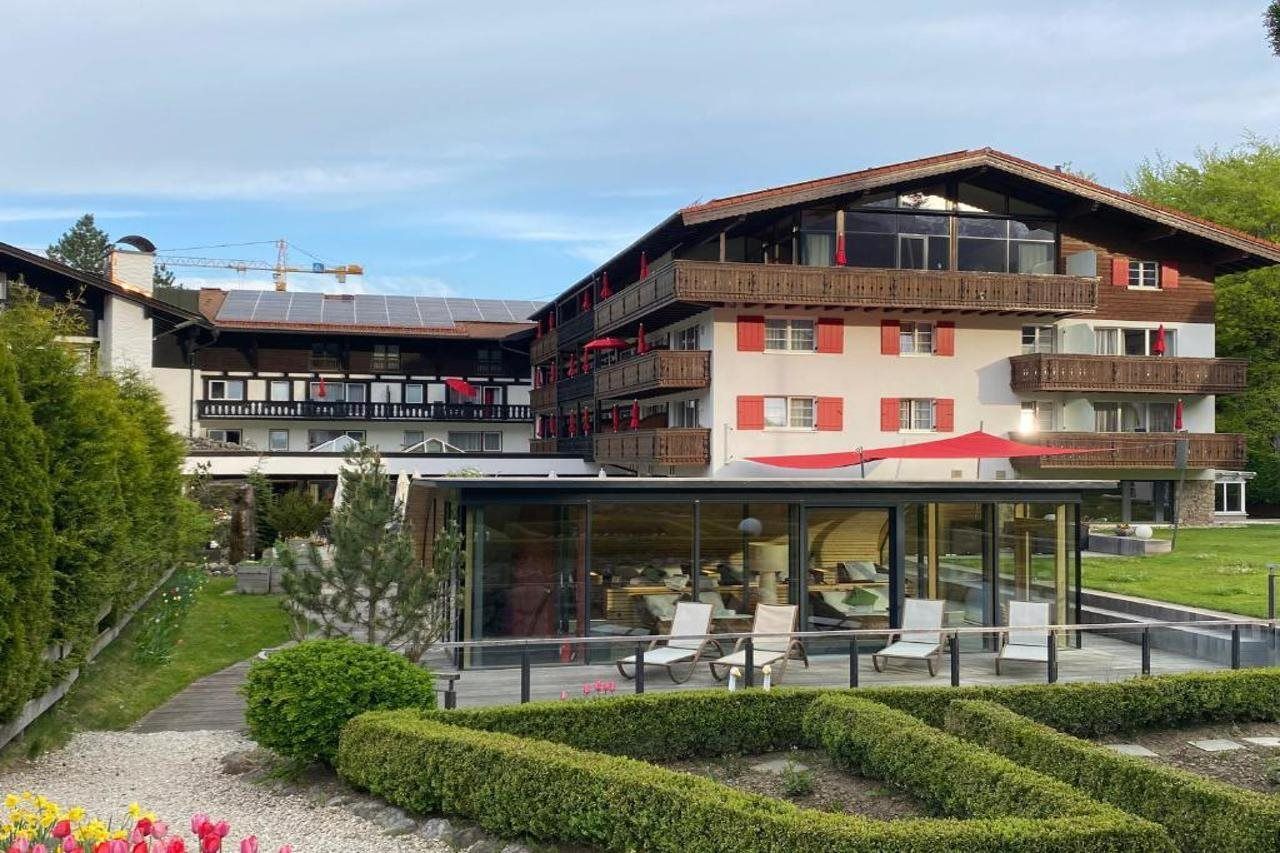 Ein mehrstöckiges Hotel mit Glasfassade, einer Sitzgelegenheit im Freien und einem gepflegten Garten.