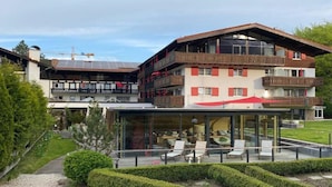 A multi-story hotel with balconies, a glass-enclosed outdoor seating area, and a well-maintained garden. - Hotel Franks (Oberstdorf)