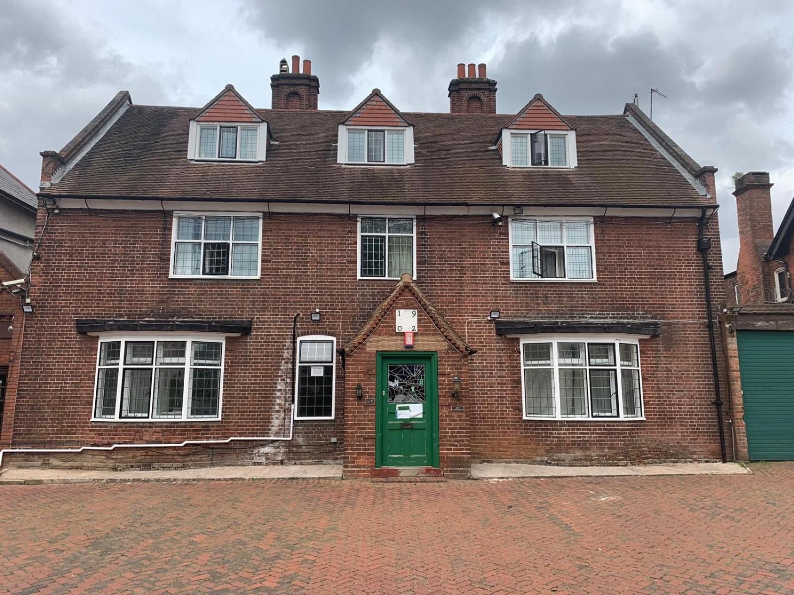 A two-story brick house with a green door, multiple windows, and a brick chimney.