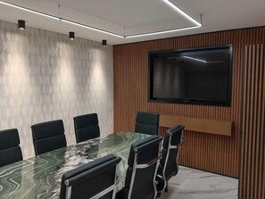 A conference room with a glass table, black chairs, a flat-screen TV, and wooden paneling on the walls. - Expo Satelite Hotel and Suites (Guadalajara)