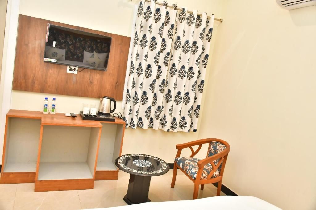 A room with a wooden desk, a round table, a chair, a television mounted on the wall, and a patterned curtain.