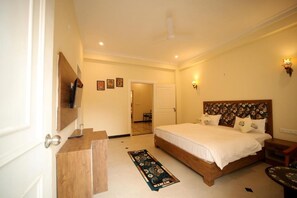 A bedroom with a bed, bedside table, a mirror, a dresser, a rug, and a door leading to another room. - Arti's Homestay (Agra)