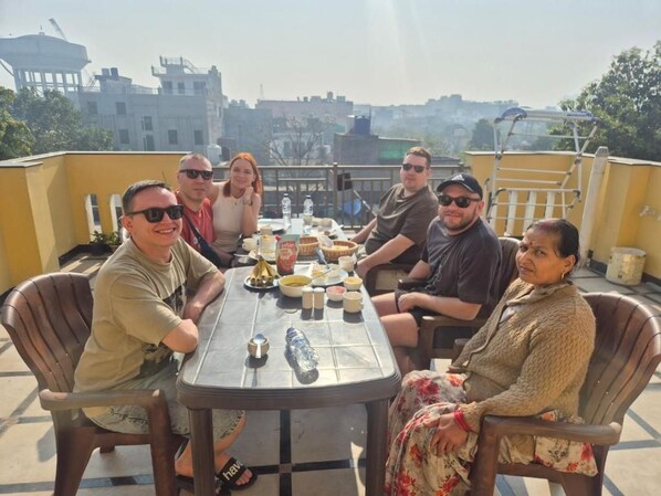 Un groupe de personnes est assis autour d’une table sur une terrasse en toit, avec une vue sur la ville en arrière-plan.
