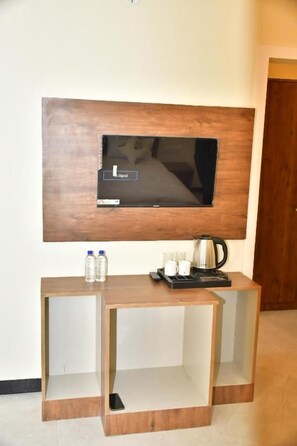 Une chambre d’hôtel avec un téléviseur fixé au mur, une console en bois sur laquelle se trouve un plateau avec divers objets, et une porte visible au fond.
