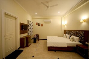 A bedroom with a bed, a television, a ceiling fan, and a wall-mounted air conditioner. - Arti's Homestay (Agra)