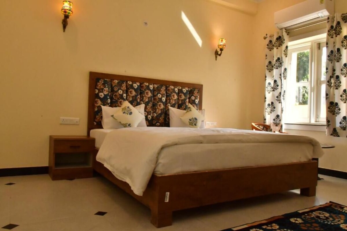 A bedroom with a wooden bed, two bedside tables, a nightstand, and a window with patterned curtains.