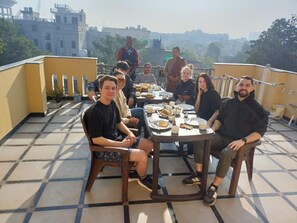 A group of people seated around a table on a rooftop terrace with a cityscape view. - Arti's Homestay (Agra)