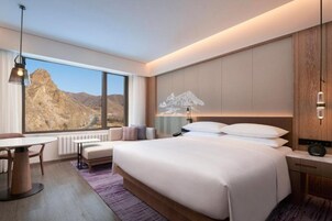Una habitación de hotel moderna con una cama grande, un área de comedor y vistas a un paisaje montañoso.