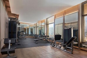 Une salle de sport équipée de divers appareils d’exercice, dotée de grandes fenêtres et d’un mur entièrement recouvert de miroirs.