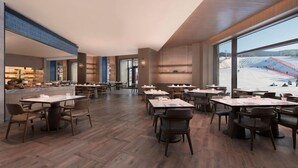 A spacious dining area with multiple tables and chairs, large windows offering a view of a snowy landscape, and a modern interior design. - Courtyard By Marriott Chongli (Zhangjiakou)