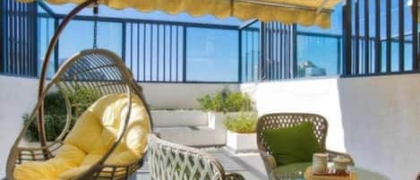 A balcony with wicker furniture, including a hanging chair and a table with a cushion.