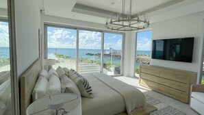 Quarto moderno com cama grande, televisão e vista para o mar.