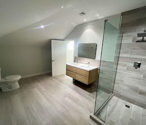 Ein modernes Badezimmer mit Duschkabine aus Glas, einem Holzkosmetikschrank und einer weißen Toilette.