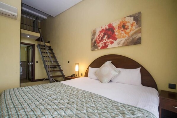 A hotel room with a bed, a painting on the wall, a staircase, and a nightstand with a lamp. - Taarifa Suites (Nairobi)