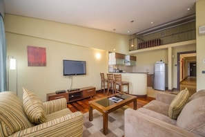 A living room with a TV, sofa, and coffee table. There is a kitchen area with cabinets and a refrigerator. - Taarifa Suites (Nairobi)