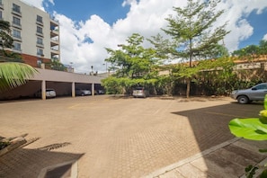 A parking area with a covered structure, trees, and a building in the background. - Taarifa Suites (Nairobi)