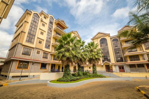 A multi-story hotel with a central courtyard, featuring palm trees and a paved walkway. - Kengen RBS Gardens Apartments (Nairobi)