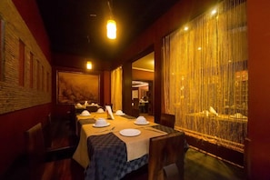 A restaurant with a long table set for dining, a painting on the wall, and a curtain with vertical lines. - Kengen RBS Gardens Apartments (Nairobi)