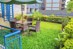 An outdoor seating area with a table and chairs, surrounded by greenery and a blue railing. - Kengen RBS Gardens Apartments (Nairobi)