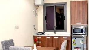 A compact kitchen with a microwave, refrigerator, and a dining area with a table and chairs. - Salsbil Almasi (Madinah)